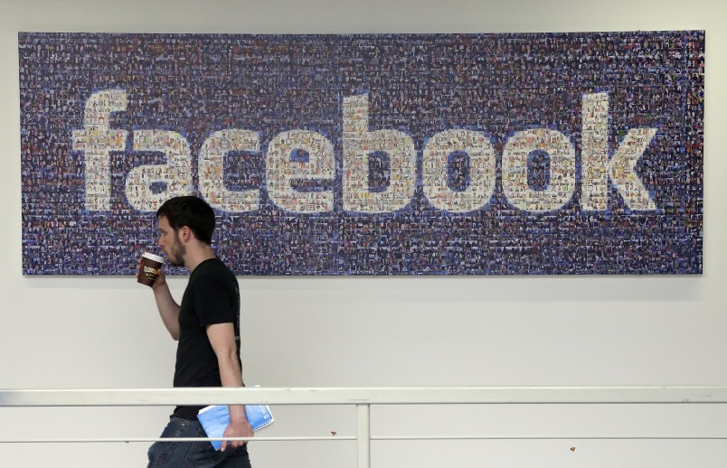 FILE - In this March 15, 2013, file photo, a Facebook employee walks past a sign at Facebook headquarters in Menlo Park, Calif. Facebook reports financial results on Wednesday, April 27, 2016. (AP Photo/Jeff Chiu, File)