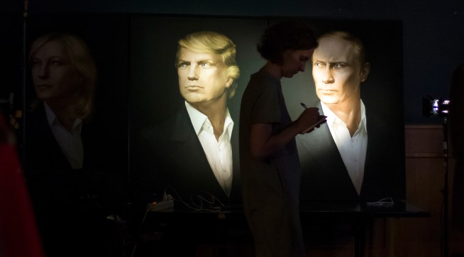 A journalist  writes a material as she watches a live telecast of the U.S. presidential election standing at portraits of Hillary Clinton, Donald Trump and Vladimir Putin in the Union Jack pub in Moscow, Russia, Wednesday, Nov. 9, 2016. Russia's lower house of parliament is applauding the election of Donald Trump as U.S. president. (AP Photo/Alexander Zemlianichenko)