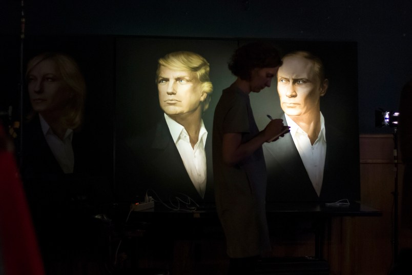 A journalist  writes a material as she watches a live telecast of the U.S. presidential election standing at portraits of Hillary Clinton, Donald Trump and Vladimir Putin in the Union Jack pub in Moscow, Russia, Wednesday, Nov. 9, 2016. Russia's lower house of parliament is applauding the election of Donald Trump as U.S. president. (AP Photo/Alexander Zemlianichenko)