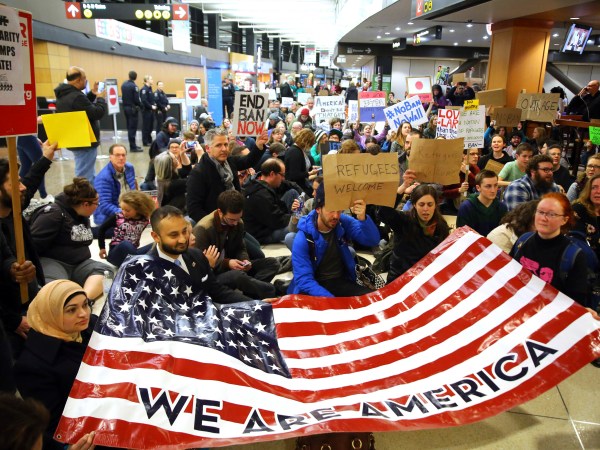Demonstrators sit down in the concourse and hold a sign that reads "We are America." More than 1,000 people gather at Seattle-Tacoma International Airport, Saturday, January 28 to protest President Trump's immigration ban.President Trump signed an executive order Friday that bars citizens from Iraq, Syria, Iran, Libya, Somalia, Sudan and Yemen from entering the U.S. for the next 90 days and suspends the admission of all refugees for 120 days. (AP Photo/seattlepi.com, Genna Martin)
