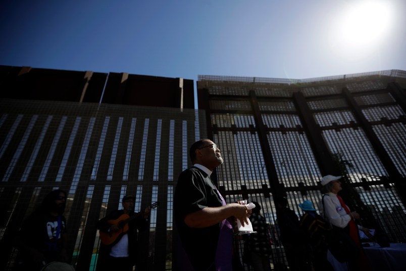 In this April 3, 2017 image, Reverend Guy A. Leemhuis, center, of the Holy Faith Episcopal Church of Los Angeles, leads a song in front of the border fence separating Tijuana, Mexico, from San Diego, in San Diego. With bids due Tuesday, April 4, 2017, on the first design contracts, companies are preparing for the worst if they get the potentially lucrative but controversial job. Four to 10 bidders are expected to be asked to build prototypes on a roughly quarter-mile (400-meter) strip of federally-owned land in San Diego, according to a U.S. official with knowledge of the plans who spoke on condition of anonymity because they haven't been made public. The land extends up to 120 feet (37 meters) from the border, raising the possibility of protests on both sides of the border.  (AP Photo/Gregory Bull)