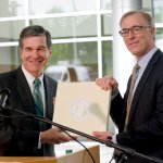 North Carolina Gov. Roy Cooper, left, and Wilson Ervin, Chair of the Credit Suisse Americas Foundation pose with the State Seal during a news conference at Credit Suisse in Morrisville, N.C., Tuesday, May 9, 2017. Credit Suisse plans to add up to 1200 jobs at its North Carolina technology hub. The jobs projection comes five weeks after North Carolina partially repealed a state law limiting LGBT rights. (AP Photo/Gerry Broome)