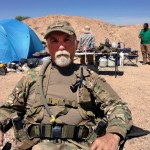 FILE - In this April 16, 2014 file photo, Jerry DeLemus, of Rochester, N.H., sits with a group of self-described militia members camping on rancher Cliven Bundy’s ranch near Bunkerville, Nev. Delemus one of two defendants are set to become the first to plead guilty in Nevada to federal charges stemming from an armed confrontation with U.S. land management agents near Nevada rancher Cliven Bundy’s ranch in 2014.DeLemus of New Hampshire is expected to enter his plea Tuesday, Aug. 23. (AP Photo/Ken Ritter, File)