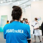 New York, NY - 5 May 2017. The opening day of the Frieze Art Fair, showcasing modern and contemporary art presented by galleries from around the world, on Randall's Island in New York City. A woman wears a T-shirt captioned "#SAVEtheNEA," as part of a movement to fight cuts in funding for the National Endowment for the Arts.
