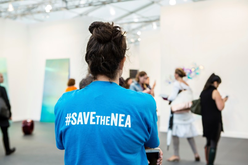 New York, NY - 5 May 2017. The opening day of the Frieze Art Fair, showcasing modern and contemporary art presented by galleries from around the world, on Randall's Island in New York City. A woman wears a T-shirt captioned "#SAVEtheNEA," as part of a movement to fight cuts in funding for the National Endowment for the Arts.