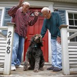 HOLD FOR EARLY RISER SUNDAY JULY 2, 2017 WITH STORY BY DAVID SHARP - In this Friday, June 30, 2017 photo 86-year-old Richard Prekins, right, Robert Maurais and their labradoodle "Scamp" outside their home in Ogunquit, Maine. Politicians have been chipping away at funding for heating aid to low-income Americans for a decade. Now President Donald Trump has proposed ending it altogether, eliciting an outcry from low-income residents who depend on the program to stay warm. (AP Photo/Stephan Savoia)