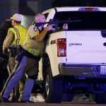 A police officer takes cover behind a truck at the scene of a shooting near the Mandalay Bay resort and casino on the Las Vegas Strip, Sunday, Oct. 1, 2017, in Las Vegas. (AP Photo/John Locher)