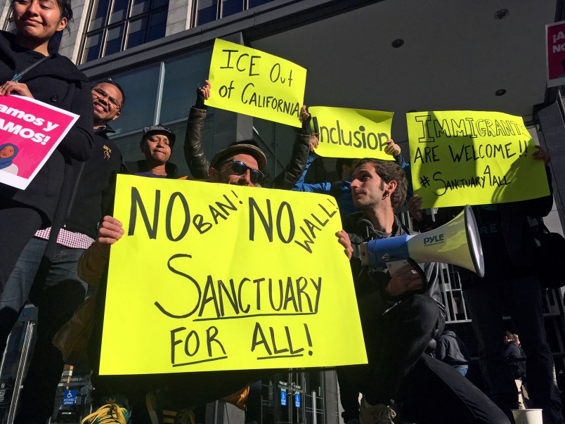 FILE - In this April 14, 2017, file photo, protesters hold up signs outside a courthouse where a federal judge was to hear arguments in the first lawsuit challenging President Donald Trump's executive order to withhold funding from communities that limit cooperation with immigration authorities in San Francisco.  A federal judge Monday, Nov. 20, 2017 has permanently blocked President Donald Trump's executive order to cut funding from cities that limit cooperation with U.S. immigration authorities. San Francisco and Santa Clara County had filed lawsuits. (AP Photo/Haven Daley, File)