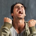 A young man yelling in frustration with his eyes closed