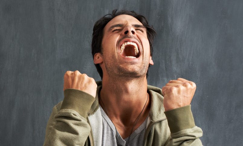 A young man yelling in frustration with his eyes closed