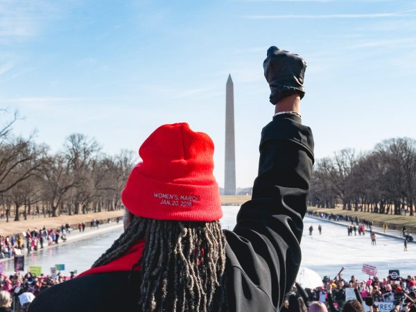 A woman stands on the steps of the Lincoln Memorial, facing the crowd and the Washington Monument, holding her fist up, and wearing a knitted cap with "Women's March Jan. 20, 2018" imprinted on it. People gathered around the reflecting pool for the "Women's March on Washington 2018", on Saturday, January 20, 2018. (Photo by Cheriss May) (Photo by Cheriss May/NurPhoto)