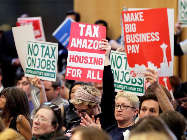 People attending a Seattle City Council meeting hold signs that read "Tax Amazon, Housing for All," and "No Tax on Jobs" listen to public comment on the debate over a possible council vote whether or not to repeal of a tax on large companies such as Amazon and Starbucks that was intended to combat a growing homelessness crisis, Tuesday, June 12, 2018, at City Hall in Seattle. (AP Photo/Ted S. Warren)