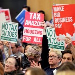 People attending a Seattle City Council meeting hold signs that read "Tax Amazon, Housing for All," and "No Tax on Jobs" listen to public comment on the debate over a possible council vote whether or not to repeal of a tax on large companies such as Amazon and Starbucks that was intended to combat a growing homelessness crisis, Tuesday, June 12, 2018, at City Hall in Seattle. (AP Photo/Ted S. Warren)