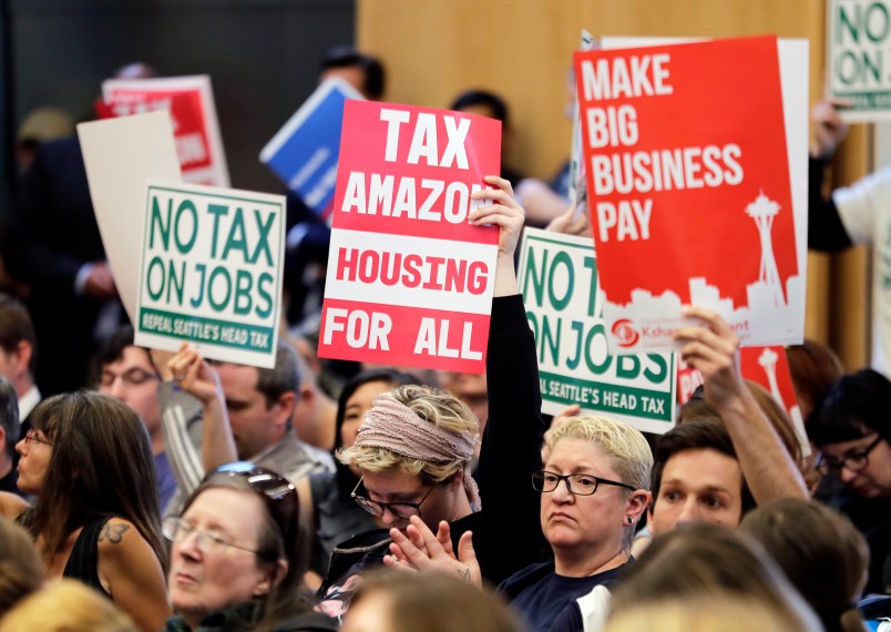 People attending a Seattle City Council meeting hold signs that read "Tax Amazon, Housing for All," and "No Tax on Jobs" listen to public comment on the debate over a possible council vote whether or not to repeal of a tax on large companies such as Amazon and Starbucks that was intended to combat a growing homelessness crisis, Tuesday, June 12, 2018, at City Hall in Seattle. (AP Photo/Ted S. Warren)