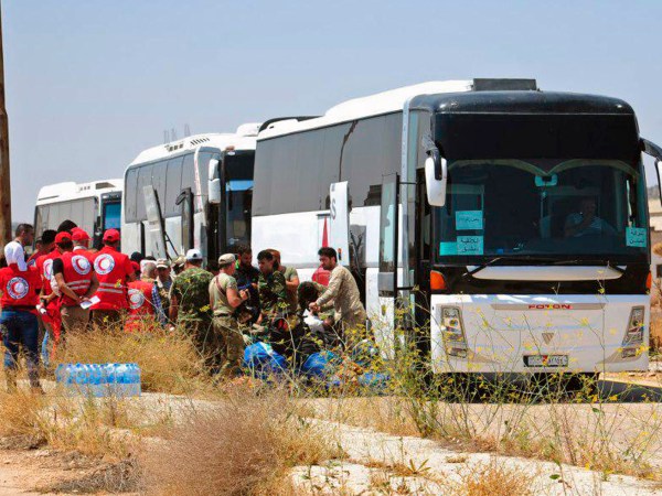 In this photo released by the Syrian official news agency SANA, ﻿Syrian government forces and Syrian Arab Red Crescent oversee the evacuation by buses of opposition fighters and their families from the southern province of Daraa, Syria, Sunday, July 15, 2018. The evacuation deal will hand over areas held by the rebels for years back to government control. Daraa, which lies on a highway linking Damascus with Jordan, was the cradle of the 2011 uprising against Syrian President Bashar Assad. (SANA via AP)