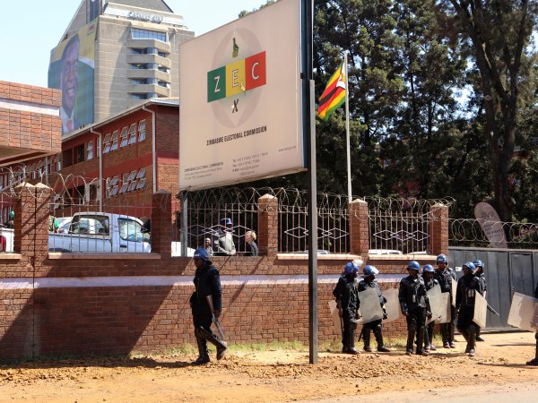 A portrait of Zimbabwean President Emmerson Mnangagawa is seen at the party headquarters as police  walk past the Zimbabwe Electoral Commission offices after  they blocked dozens of opposition party supporters  from entering the  commission offices in  Harare,  Zimbabwe,Wednesday, Aug, 1, 2018. Zimbabweans are awaiting the  first results from an election that they hope will lift the country out of economic and poltical stagnation  after decades of  rule by former leader Robert Mugabe (AP Photo/Tsvangirayi Mukwazhi)