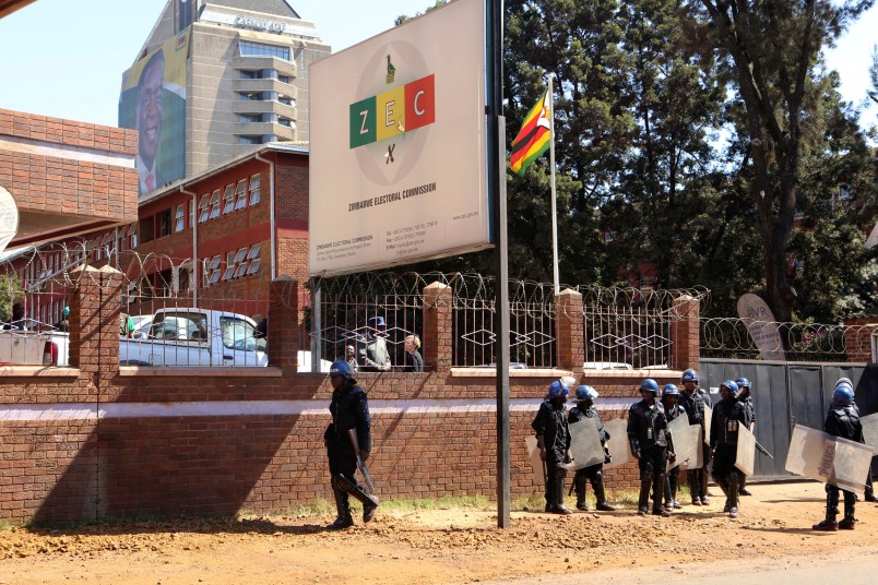 A portrait of Zimbabwean President Emmerson Mnangagawa is seen at the party headquarters as police  walk past the Zimbabwe Electoral Commission offices after  they blocked dozens of opposition party supporters  from entering the  commission offices in  Harare,  Zimbabwe,Wednesday, Aug, 1, 2018. Zimbabweans are awaiting the  first results from an election that they hope will lift the country out of economic and poltical stagnation  after decades of  rule by former leader Robert Mugabe (AP Photo/Tsvangirayi Mukwazhi)