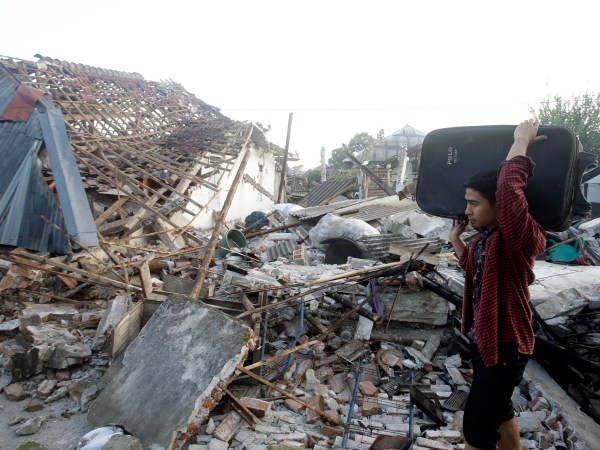 A man carries his belonging pass ruin houses at a village affected by Sunday's earthquake in North Lombok, Indonesia, Thursday, Aug. 9, 2018. The north of Lombok has been devastated by the magnitude 7.0 quake that struck Sunday night, damaging thousands of buildings and killing a large number of people. (AP Photo/Firdia Lisnawati)