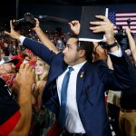A staff member for President Donald Trump blocks a camera as a photojournalist attempts to take a photo of a protester during a campaign rally at Ford Center, Thursday, Aug. 30, 2018, in Evansville, Ind. (AP Photo/Evan Vucci)