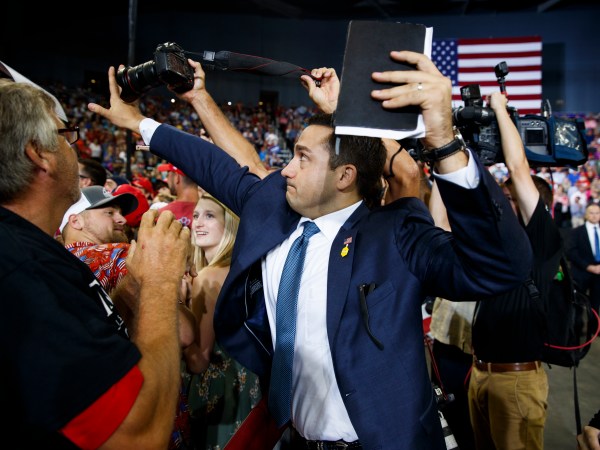 A staff member for President Donald Trump blocks a camera as a photojournalist attempts to take a photo of a protester during a campaign rally at Ford Center, Thursday, Aug. 30, 2018, in Evansville, Ind. (AP Photo/Evan Vucci)
