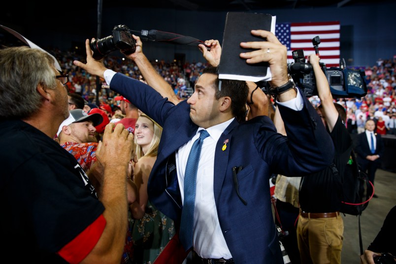 A staff member for President Donald Trump blocks a camera as a photojournalist attempts to take a photo of a protester during a campaign rally at Ford Center, Thursday, Aug. 30, 2018, in Evansville, Ind. (AP Photo/Evan Vucci)
