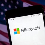 KIEV, UKRAINE - 2018/08/06: The Microsoft logo seen displayed on a smart phone with a background of an American Flag. According to the New York Stock Exchange (NYSE), the company is on the fourth place at the market value in the world - $ 825.8 billion. (Photo by Igor Golovniov/SOPA Images/LightRocket via Getty Images)
