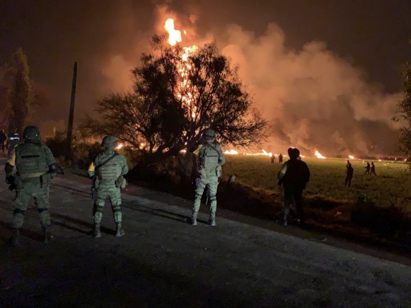 In this image provided by the Secretary of National Defense, soldiers guard the area where the explosion was recorded in Tlahuelilpan, Hidalgo state, Mexico, Friday, Jan. 18, 2019. A huge fire exploded at a pipeline leaking fuel in central Mexico on Friday, killing at least 21 people and badly burning 71 others as locals were collecting the spilling gasoline in buckets and garbage cans, officials said.The leak was caused by an illegal tap that fuel thieves had drilled into the pipeline in a small town in the state of Hidalgo, about 62 miles (100 kilometers) north of Mexico City, according to state oil company Petroleos Mexicanos, or Pemex. (Secretary of National Defense via AP)