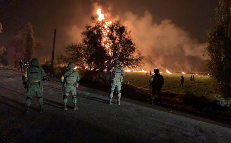 In this image provided by the Secretary of National Defense, soldiers guard the area where the explosion was recorded in Tlahuelilpan, Hidalgo state, Mexico, Friday, Jan. 18, 2019. A huge fire exploded at a pipeline leaking fuel in central Mexico on Friday, killing at least 21 people and badly burning 71 others as locals were collecting the spilling gasoline in buckets and garbage cans, officials said.The leak was caused by an illegal tap that fuel thieves had drilled into the pipeline in a small town in the state of Hidalgo, about 62 miles (100 kilometers) north of Mexico City, according to state oil company Petroleos Mexicanos, or Pemex. (Secretary of National Defense via AP)