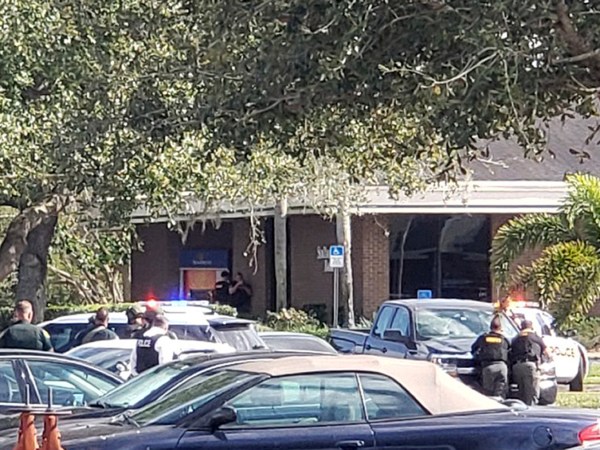 Law enforcement officials take cover outside the SunTrust Bank branch, Wednesday, Jan. 23, 2019, in Sebring, Fla. Authorities say they've arrested a man who fired shots inside the Florida bank. (Highlands NewsSun via AP)