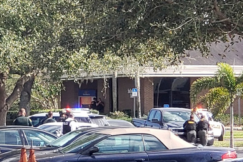 Law enforcement officials take cover outside the SunTrust Bank branch, Wednesday, Jan. 23, 2019, in Sebring, Fla. Authorities say they've arrested a man who fired shots inside the Florida bank. (Highlands NewsSun via AP)
