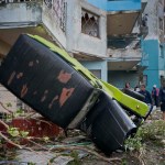 People walk next to a car overturned by the force of the tornado in Havana, Cuba, Monday, Jan. 28, 2019. A tornado and pounding rains smashed into the eastern part of Cuba's capital overnight, toppling trees, bending power poles and flinging shards of metal roofing through the air as the storm cut a path of destruction across eastern Habana.Power was cut to many areas and President Miguel Diaz-Canel said Monday at least three people were killed and 172 injured. (AP Photo/Ramon Espinosa)