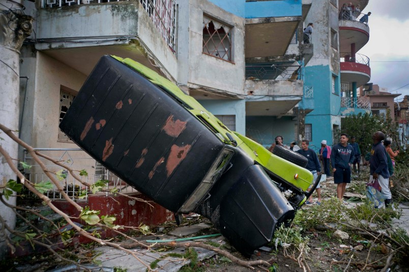 People walk next to a car overturned by the force of the tornado in Havana, Cuba, Monday, Jan. 28, 2019. A tornado and pounding rains smashed into the eastern part of Cuba's capital overnight, toppling trees, bending power poles and flinging shards of metal roofing through the air as the storm cut a path of destruction across eastern Habana.Power was cut to many areas and President Miguel Diaz-Canel said Monday at least three people were killed and 172 injured. (AP Photo/Ramon Espinosa)