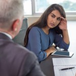 Business leader instructing focused Indian female assistant. Serious and upset woman leaning head on hand and listening to boss during coffee break. Teamwork or company hierarchy concept