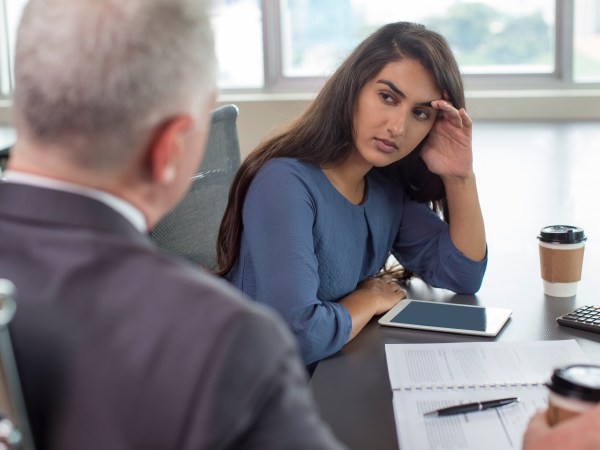 Business leader instructing focused Indian female assistant. Serious and upset woman leaning head on hand and listening to boss during coffee break. Teamwork or company hierarchy concept