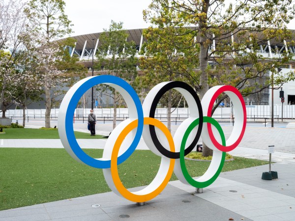 TOKYO, JAPAN, MARCH 27TH 2020 - Am man wearing protective mask stands by the Olympic logo at the new National Stadium built for the 2020 Olympics that have just be posponed to 2021 due to coronavirus outbreak