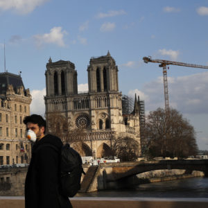 A masked man walks next to Notre Dame Cathedral, in Paris, Wednesday, March 18, 2020. French President Emmanuel Macron said that for 15 days people will be allowed to leave the place they live only for necessary activities such as shopping for food, going to work or taking a walk. For most people, the new coronavirus causes only mild or moderate symptoms. For some it can cause more severe illness, especially in older adults and people with existing health problems. (AP Photo/Francois Mori)