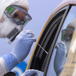 A helper of the German Red Cross DRK in protective suit, left, takes a smear from a patient in his car during the official opening of a drive-through (drive-in) COVID-19 testing center at the fair ground in Dresden, eastern Germany, Wednesday, April 15, 2020. The appointment-only drive-through testing center is starting today with working. Medical staff reache into a car to take a nasopharyngeal swab from a patient. (AP Photo/Jens Meyer)