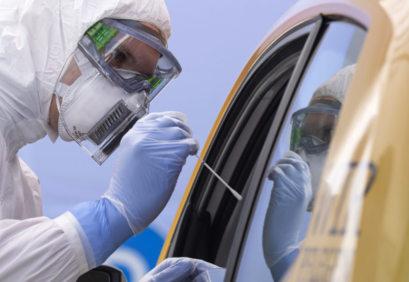 A helper of the German Red Cross DRK in protective suit, left, takes a smear from a patient in his car during the official opening of a drive-through (drive-in) COVID-19 testing center at the fair ground in Dresden, eastern Germany, Wednesday, April 15, 2020. The appointment-only drive-through testing center is starting today with working. Medical staff reache into a car to take a nasopharyngeal swab from a patient. (AP Photo/Jens Meyer)