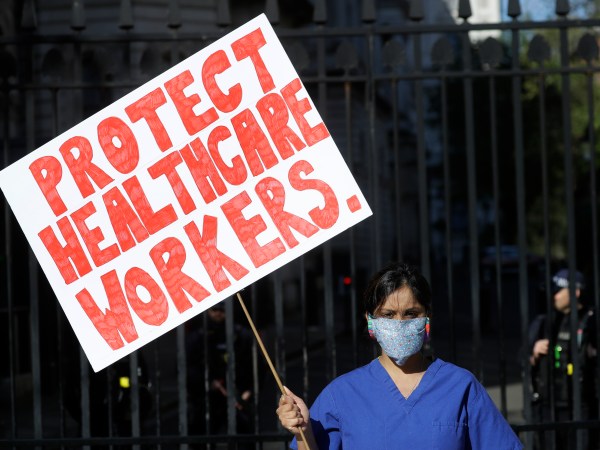 Doctor Meenal Viz holds a banner as she protests outside Downing Street in London, as the country is in lockdown to help curb the spread of the coronavirus, Sunday, April 19, 2020. The doctor who is pregnant was protesting about the lack of PPE and protection for NHS health workers. (AP Photo/Kirsty Wigglesworth)