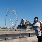 A woman wearing a protection mask walks over Westminster Bridge in London, Wednesday April 22, 2020 during the COVID-19 lockdown. (AP Photo/Frank Augstein)