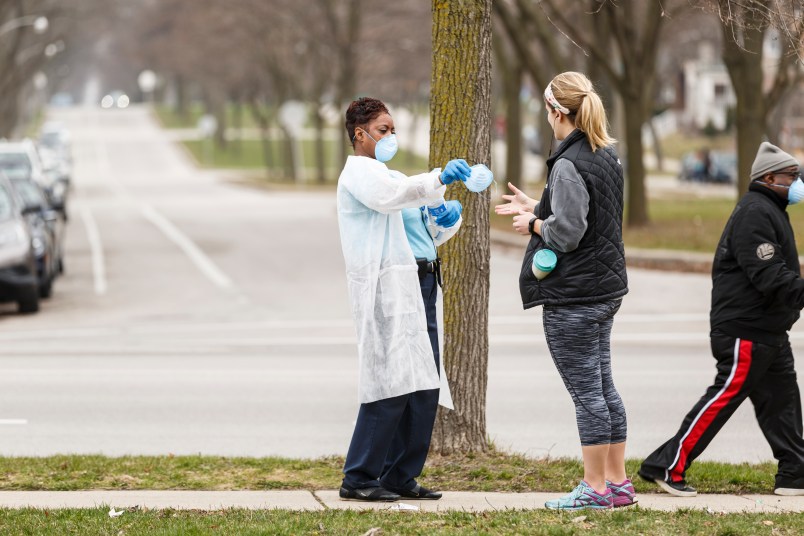 Milwaukee, WI - APRIL 7th: A woman hands out surgical masks to people standing in line to vote in Wisconsin’s spring primary election on Tuesday April 7th, 2020 at Riverside High School in Milwaukee, WI. (Photo by Sara Stathas for the Washington Post)