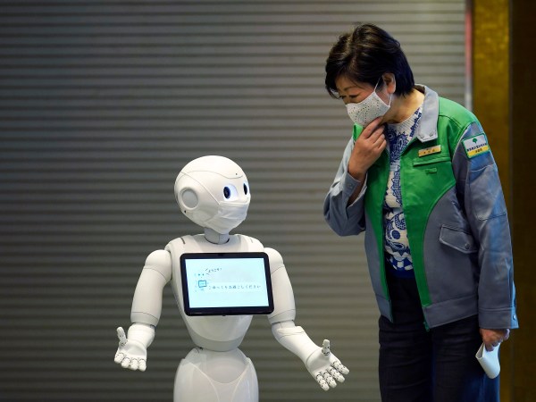 A humanoid robot Pepper with a face mask  greets Tokyo Gov. Yuriko Koike at the lobby of a hotel for the new coronavirus COVID-19 patients with mild symptoms during a media preview in Tokyo Friday, May 1, 2020. Prime Minister Shinzo Abe said Thursday he planned to extend a state of emergency beyond the scheduled end of May 6 because infections are spreading and hospitals are overburdened. (AP Photo/Eugene Hoshiko)