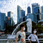 /// In this image taken Saturday, Mar. 14, 2020, a couple wearing face masks walk past the Merlion statue in Singapore. As the virus outbreak spreads ever further, it's becoming clear that some strategies are more likely to succeed in containing it: pro-active efforts to track down and isolate cases, access to basic, affordable public health and clear, reassuring messaging from leaders. (AP Photo/Ee Ming Toh)