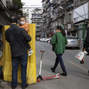 In this photo taken Wednesday, April 1, 2020, residents walk past a sealed off neighborhood in Wuhan in central China's Hubei province. Authorities in Wuhan, the Chinese city where the coronavirus pandemic first broke out, have reportedly launched a plan to test everyone in the city of 11 million people in the next 10 days.  (AP Photo/Ng Han Guan)