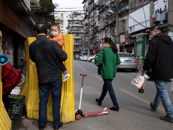 In this photo taken Wednesday, April 1, 2020, residents walk past a sealed off neighborhood in Wuhan in central China's Hubei province. Authorities in Wuhan, the Chinese city where the coronavirus pandemic first broke out, have reportedly launched a plan to test everyone in the city of 11 million people in the next 10 days.  (AP Photo/Ng Han Guan)