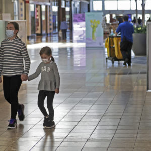 Shoppers walks past a sign encouraging masks at SouthPark Mall, Wednesday, May 13, 2020, in Strongsville, Ohio. Ohio retail businesses reopened Tuesday following a nearly two-month-long shutdown ordered by Gov. Mike DeWine to limit the spread of the coronavirus.  (AP Photo/Tony Dejak)