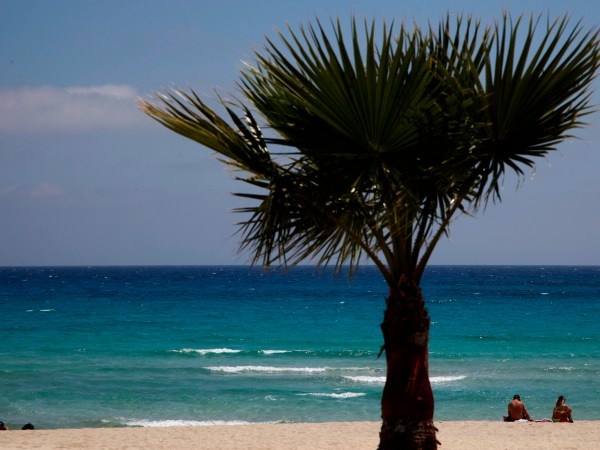 In this image taken on Sunday, May 10 2020, sunbathers sit on an empty stretch of ‘Landa’ beach at the Cyprus seaside resort of Ayia Napa, a favorite among tourists from Europe and beyond. (AP Photo/Petros Karadjias)