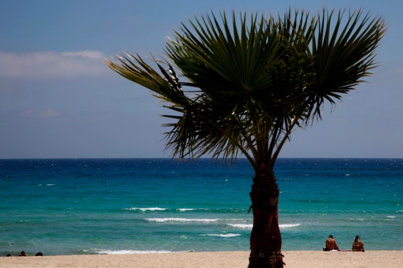 In this image taken on Sunday, May 10 2020, sunbathers sit on an empty stretch of ‘Landa’ beach at the Cyprus seaside resort of Ayia Napa, a favorite among tourists from Europe and beyond. (AP Photo/Petros Karadjias)