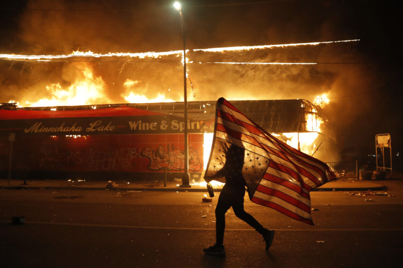 A protester carries the carries the U.S. flag upside, a sign of distress, Thursday, May 28, 2020, in Minneapolis. Violent protests over the death of George Floyd, the black man who died in police custody broke out in Minneapolis for a third straight night. (AP Photo/Julio Cortez)