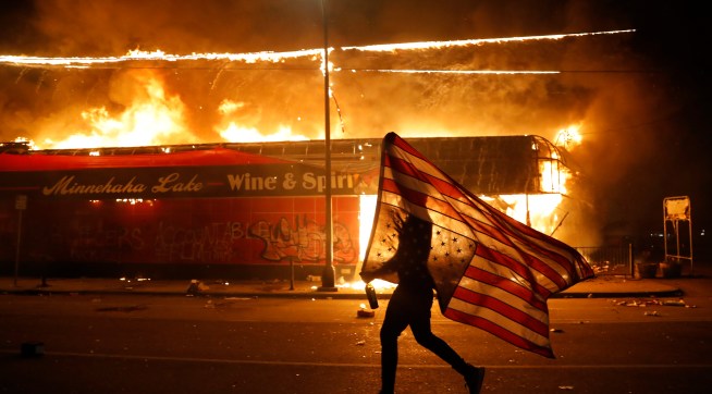 A protester carries the carries the U.S. flag upside, a sign of distress, Thursday, May 28, 2020, in Minneapolis. Violent protests over the death of George Floyd, the black man who died in police custody broke out in Minneapolis for a third straight night. (AP Photo/Julio Cortez)